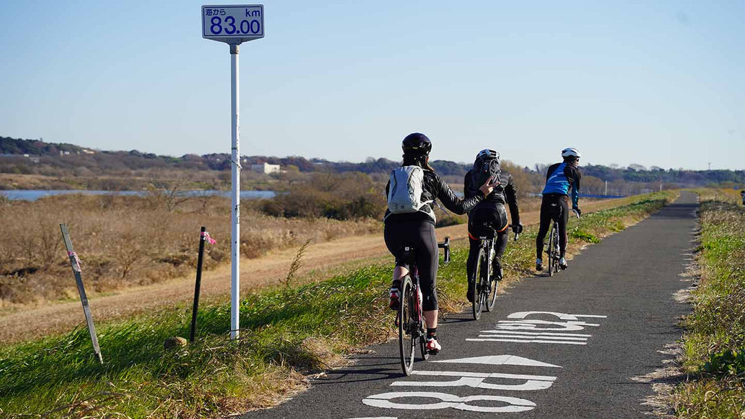 利根川サイクリングロードをロードバイクで走るスタッフの後ろ姿