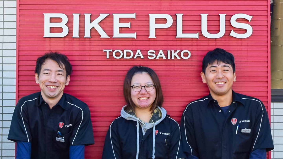 バイクプラス戸田彩湖店の大きなロゴマークの前でのスタッフ集合写真