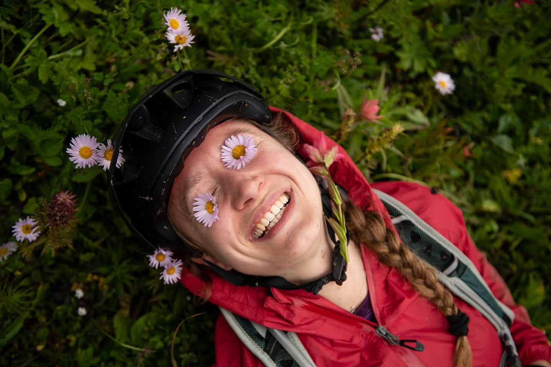 草むらに寝転び両目にピンクの花を乗せて笑う女性の写真