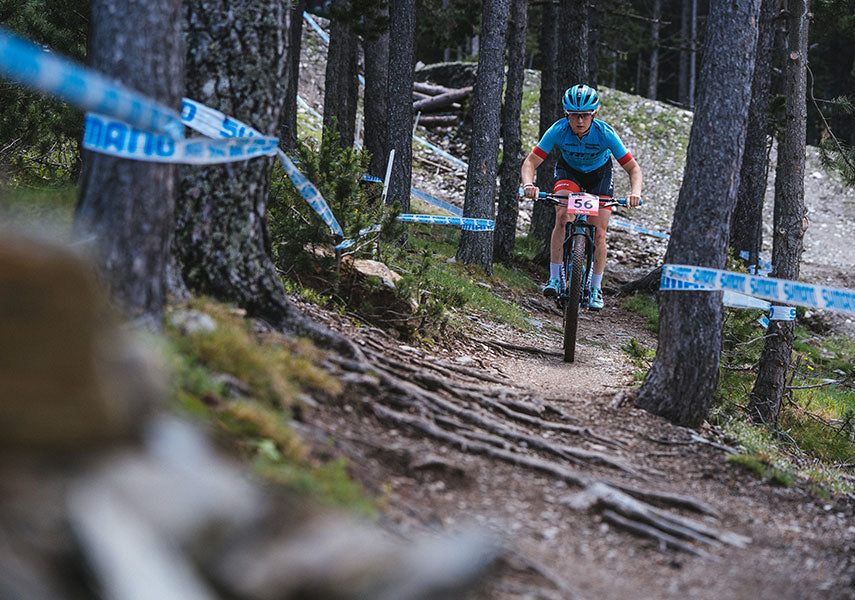 複数の木の根が剥き出しになっている斜めの滑りやすい斜面をのぼる女子クロスカントリー選手の様子