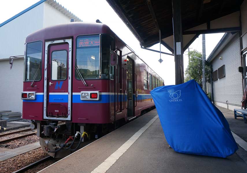 自転車が収納された輪行袋をホームに置いて電車の先頭車両が写るように撮影した写真